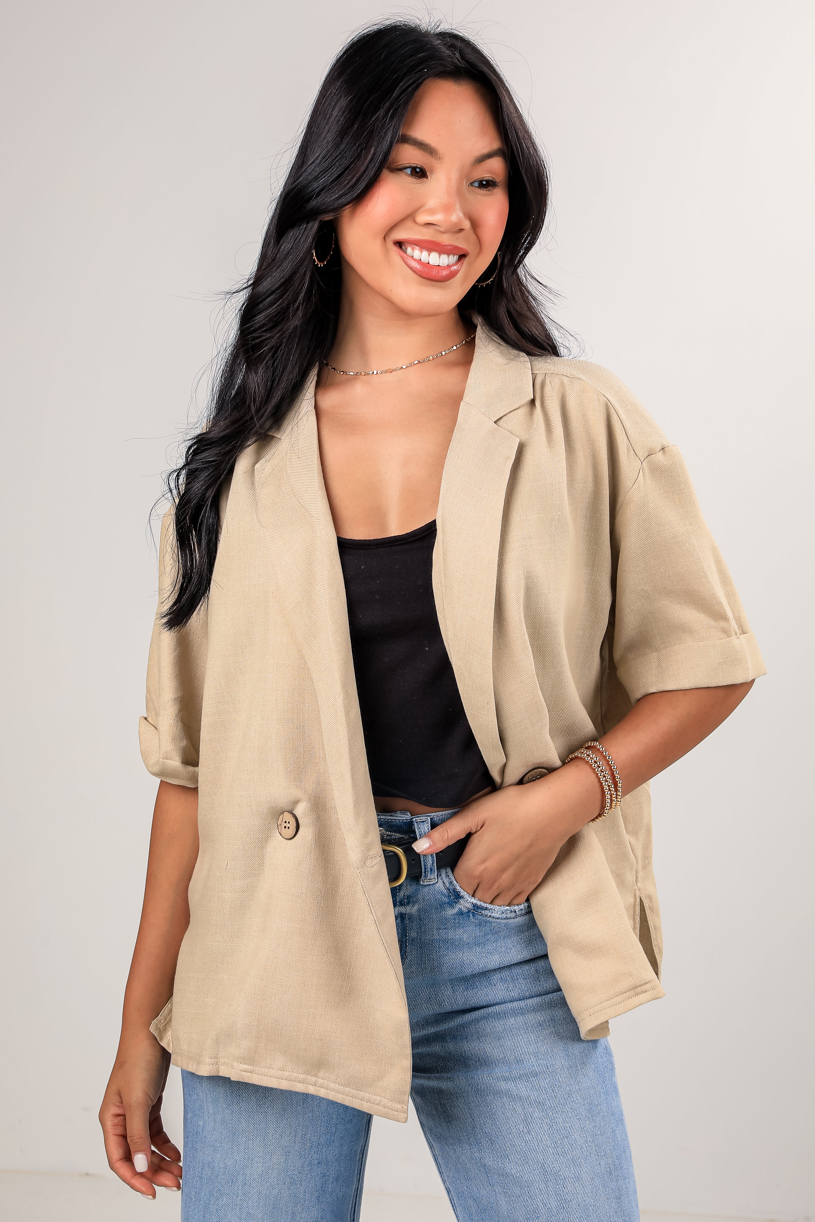 Woman wearing a beige blazer over a black top and blue jeans on a plain background