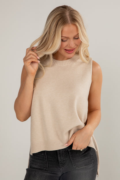 Woman wearing a beige sleeveless sweater against a plain background