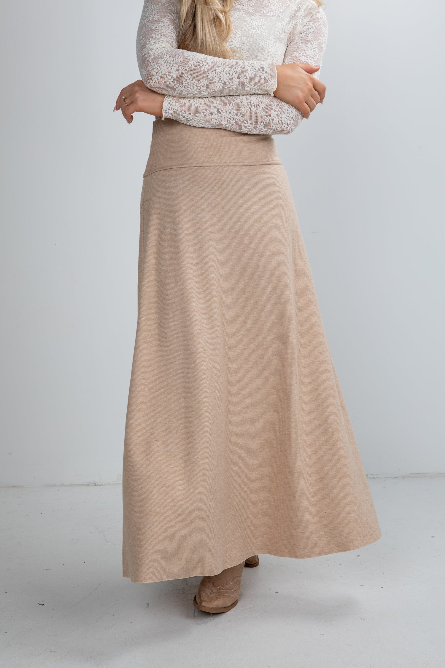 Woman wearing a beige skirt and white lace top on a light gray background