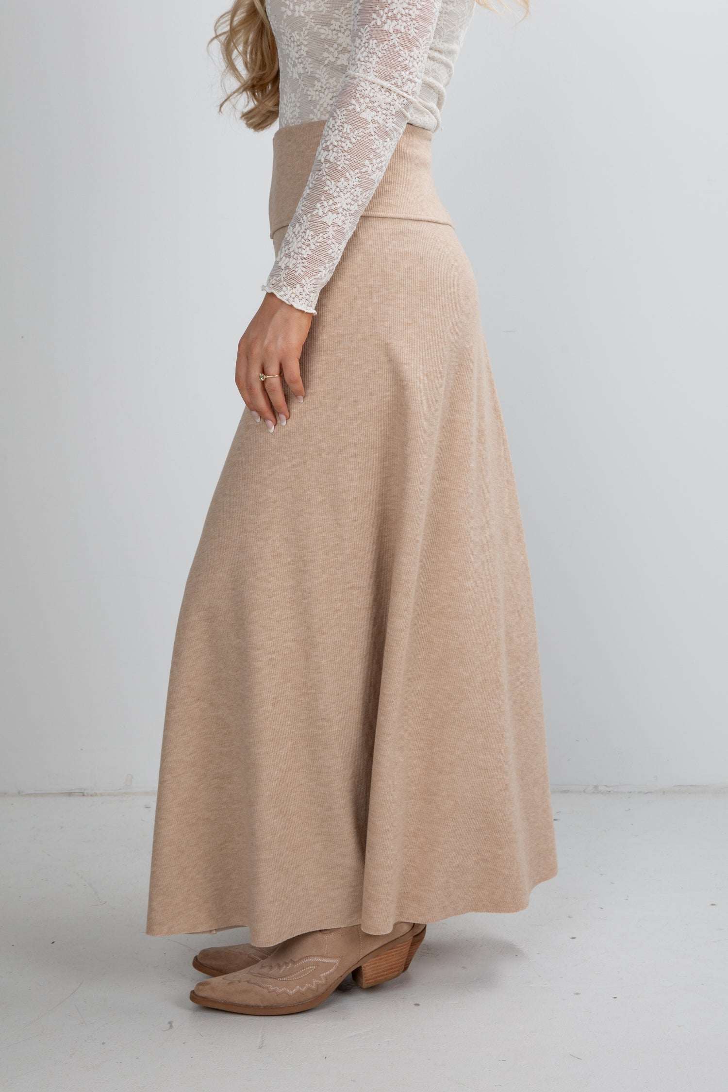 Person wearing a beige skirt and white lace top on a plain background