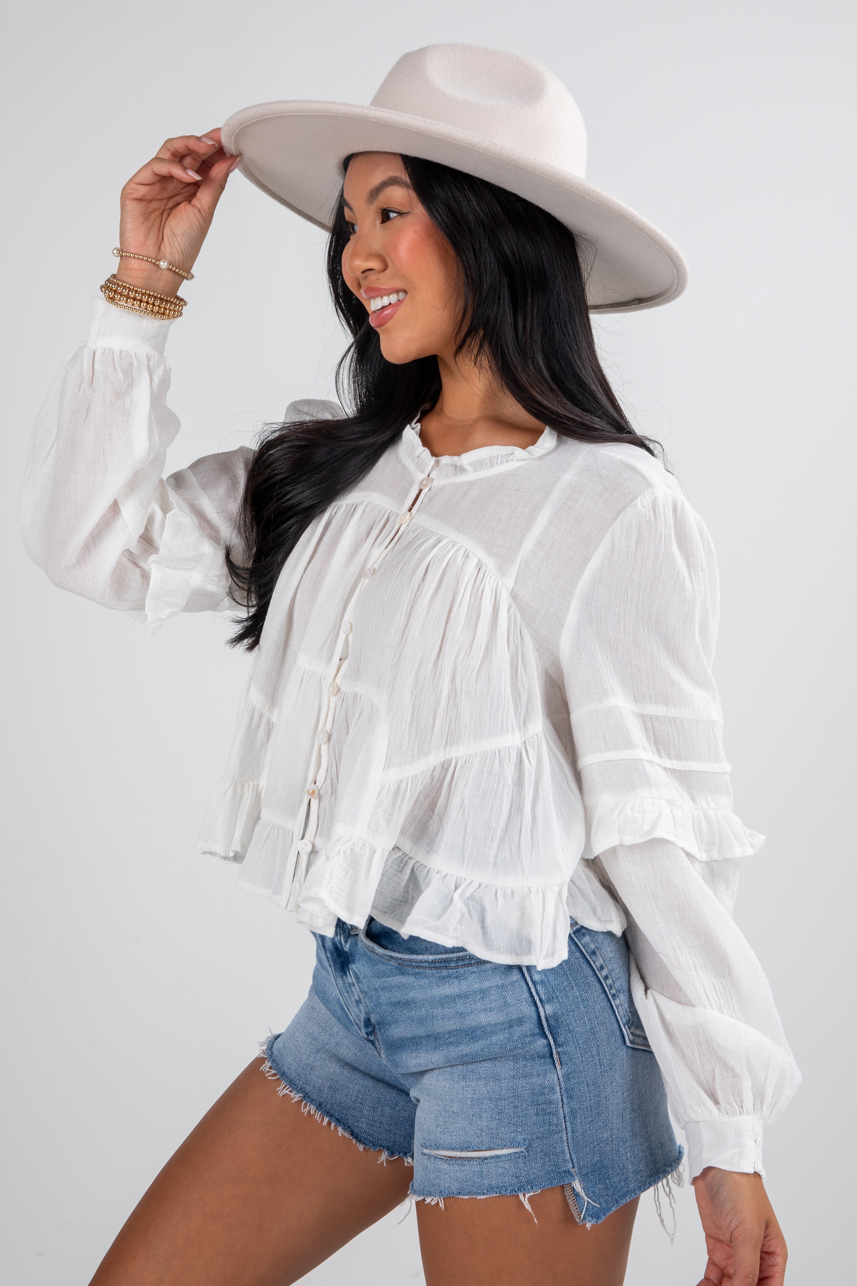 Woman wearing a white blouse, denim shorts, and a beige hat on a plain background