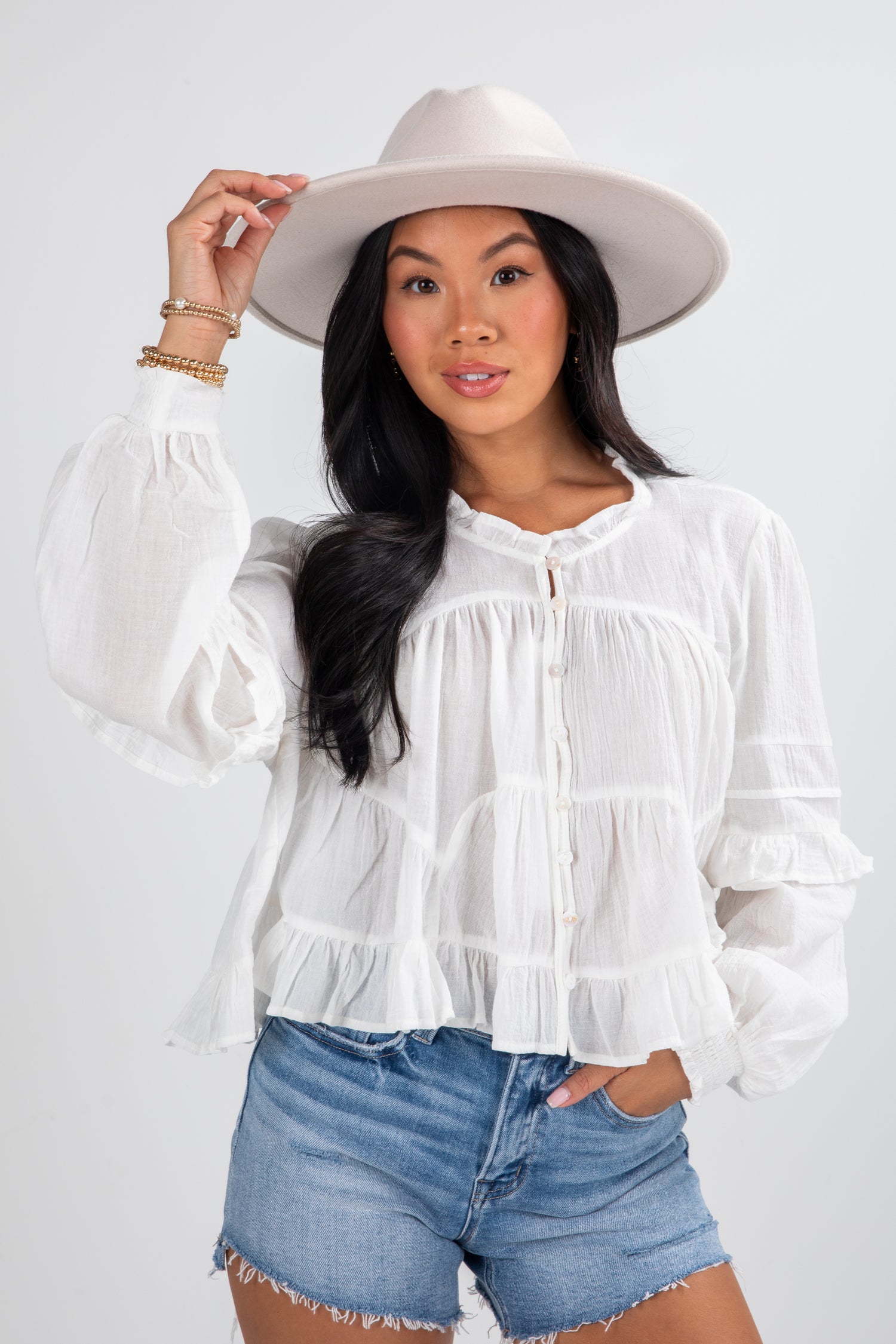 Woman wearing a white blouse, denim shorts, and a white hat on a plain background