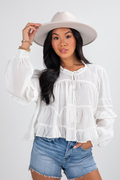 Woman wearing a white blouse, denim shorts, and a white hat on a plain background