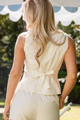 Woman wearing a light-colored sleeveless top with a bow detail outdoors.