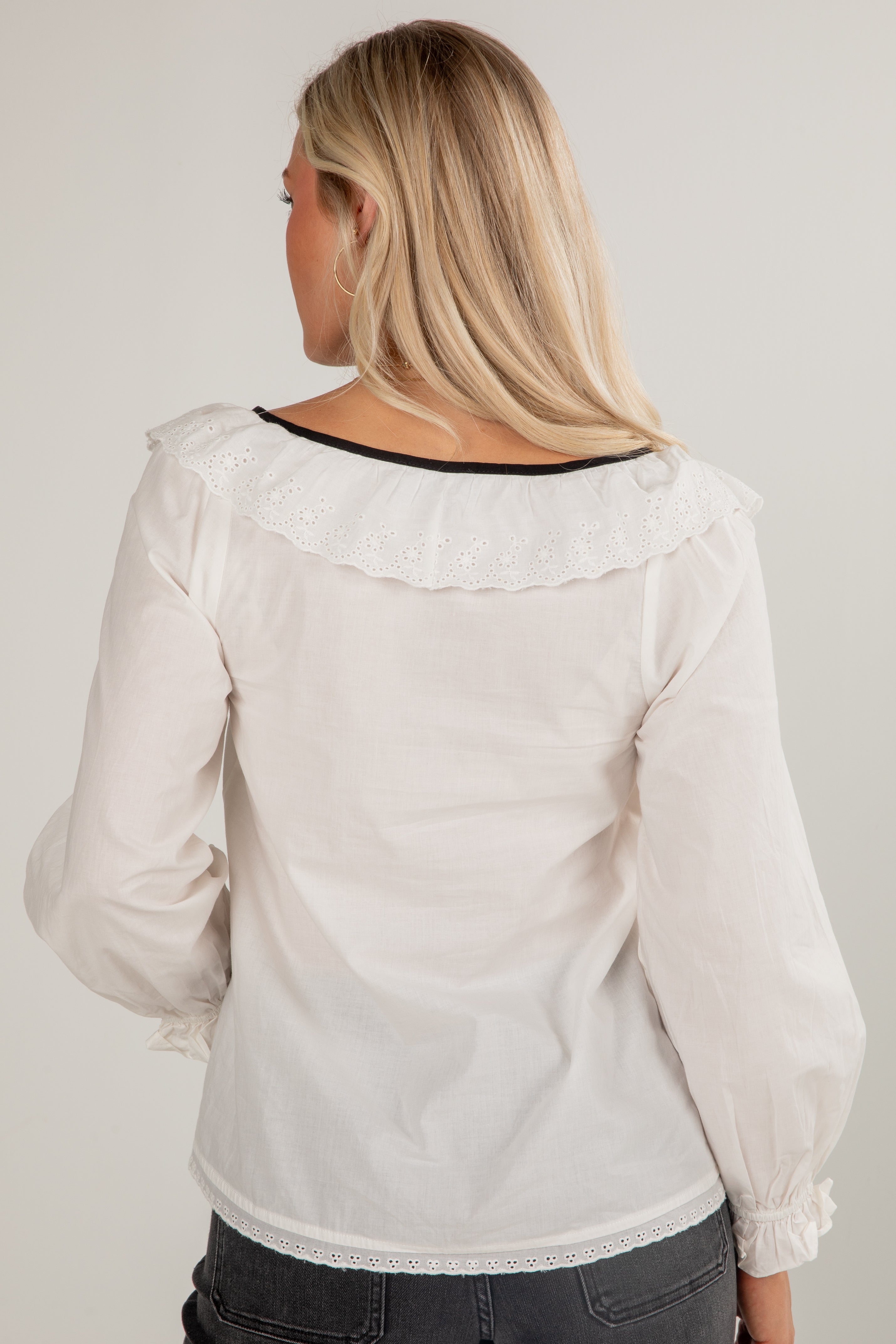 Woman wearing a white blouse with long sleeves and lace details on a plain background