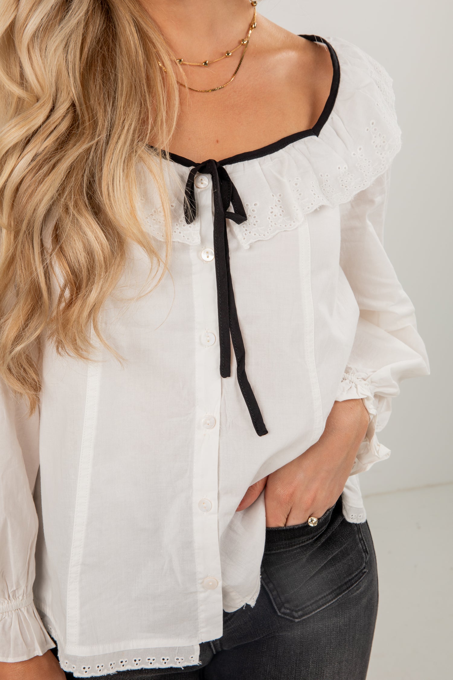 White blouse with black trim worn by a person against a white background