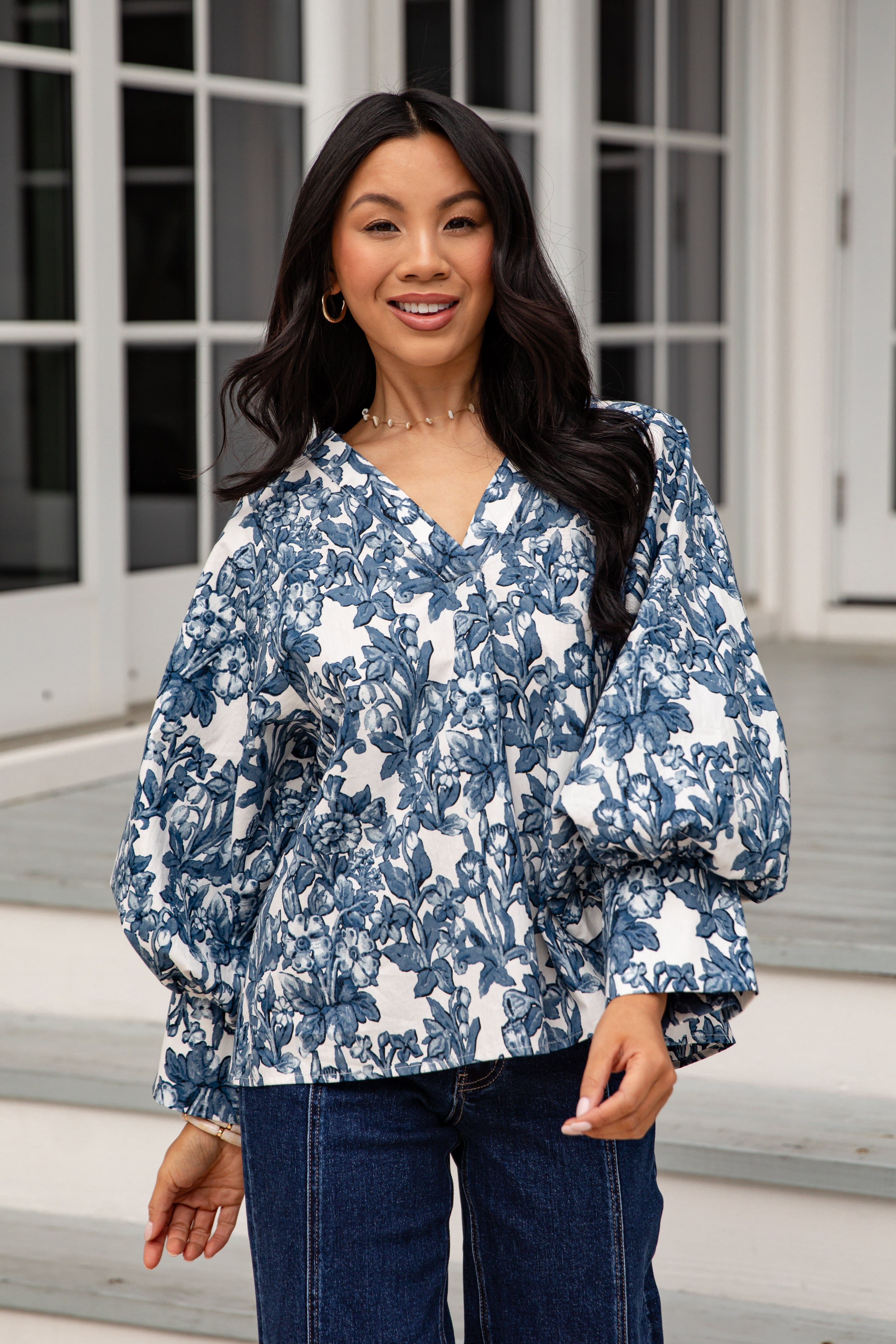 Woman wearing a blue floral blouse and jeans standing outdoors.