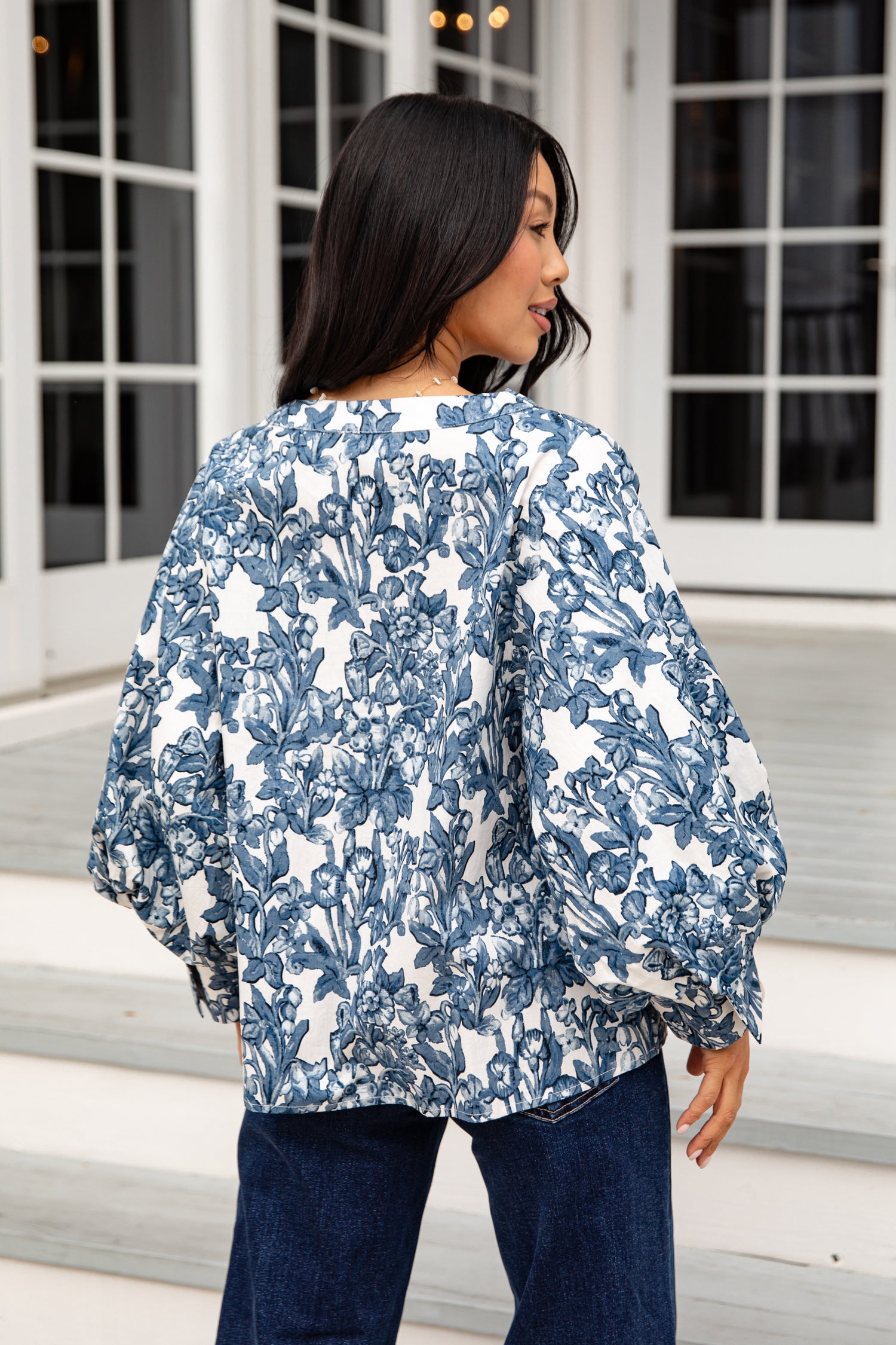 Woman wearing a blue and white floral jacket standing on steps.