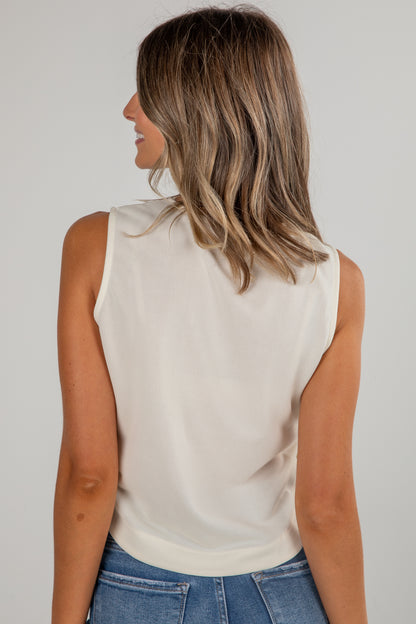 Woman wearing a beige sleeveless top and blue jeans against a plain background