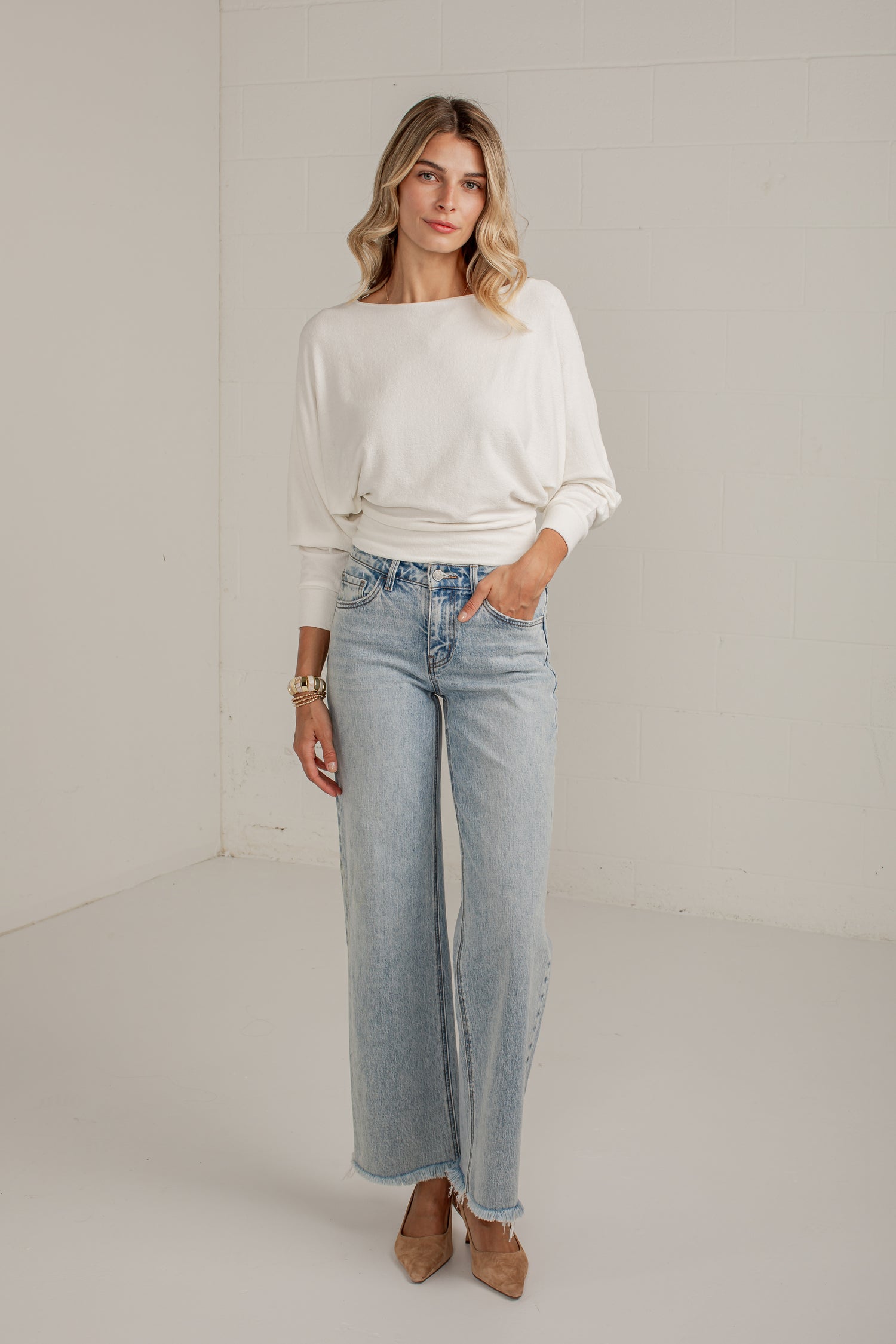 A woman modeling a white long-sleeve top and light-wash wide-leg jeans against a plain white studio background.