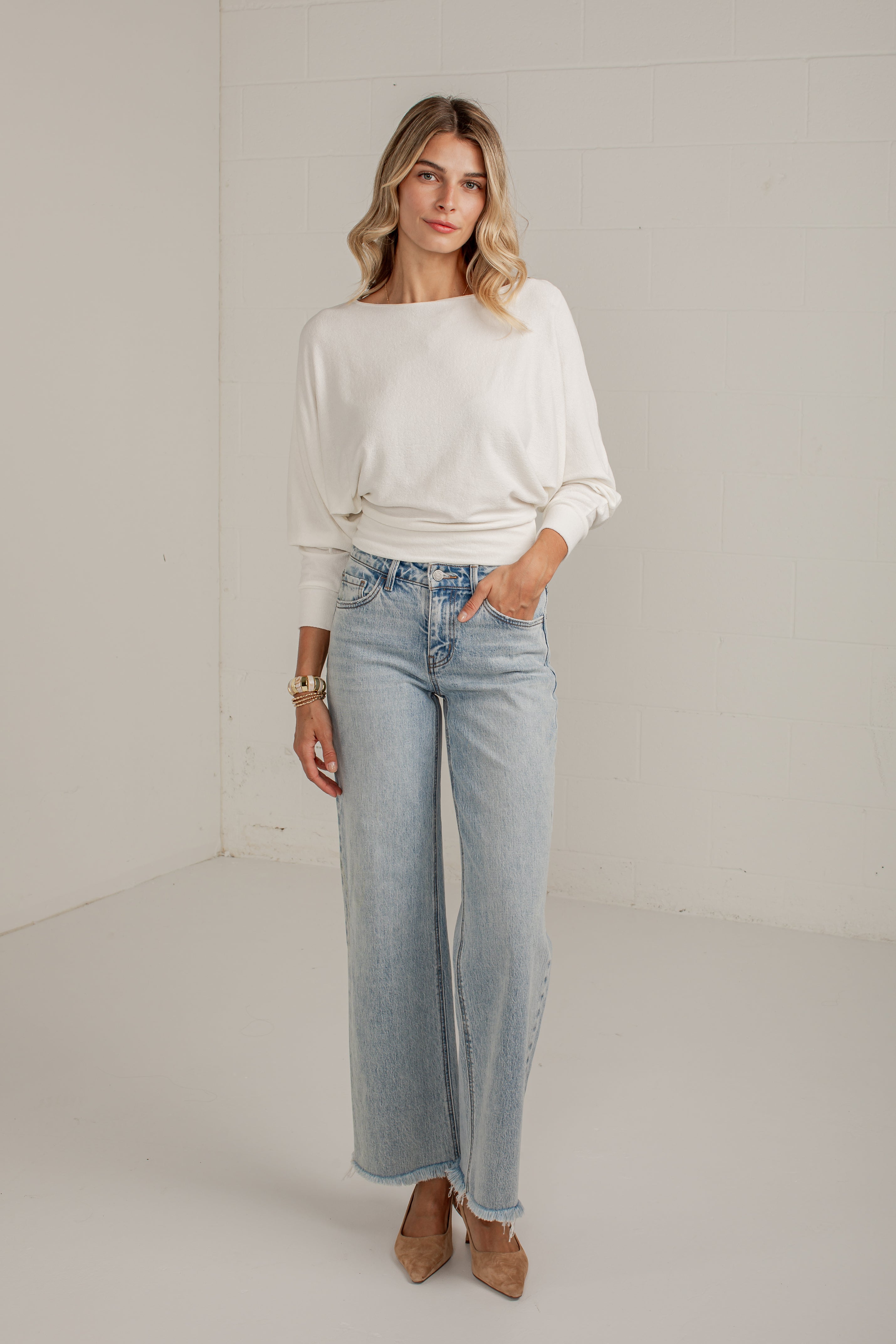 A woman modeling a white long-sleeve top and light-wash wide-leg jeans against a plain white studio background.