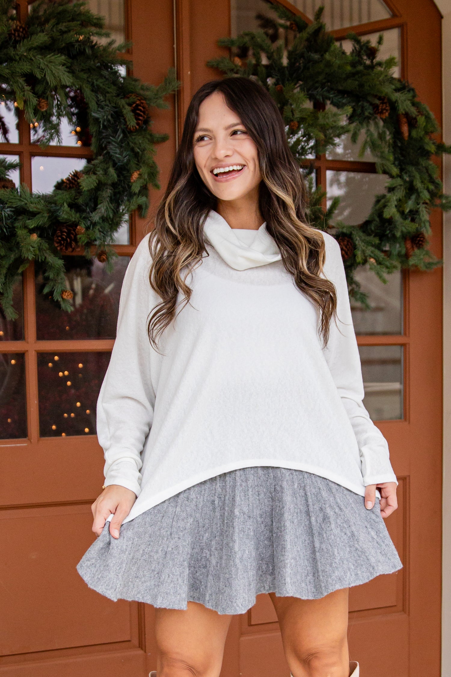 Woman wearing a white sweater and gray skirt standing in front of a decorated door.