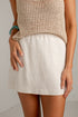 A person wearing a light beige linen mini skirt and a beige woven knit top, shown from the chest down against a plain light background.
