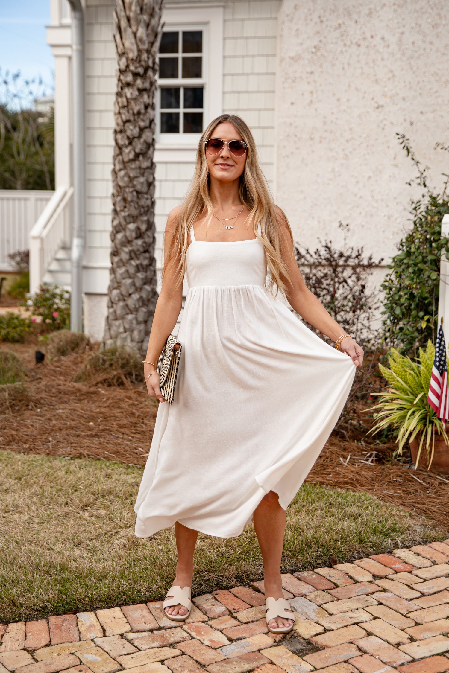 Woman in a white dress standing on a brick path in front of a white building.