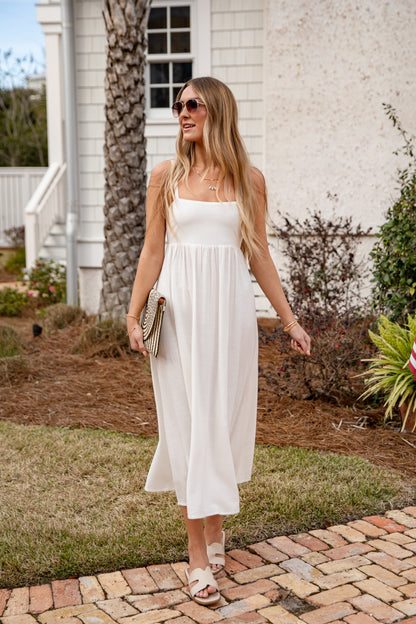 Woman in a white dress standing on a brick path in front of a house.