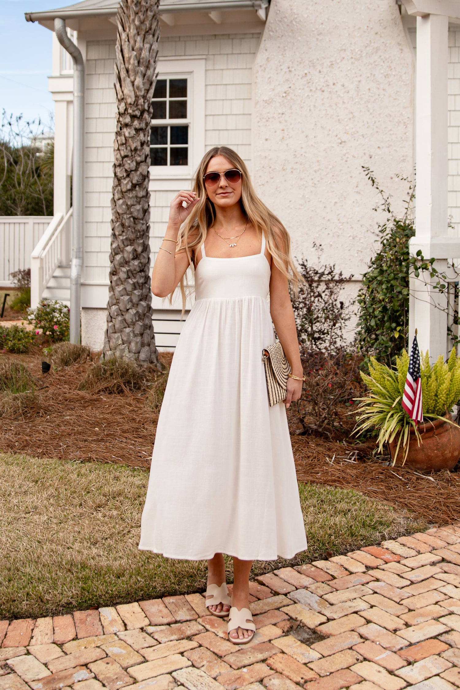 Woman in a white dress standing on a brick path in front of a white house.