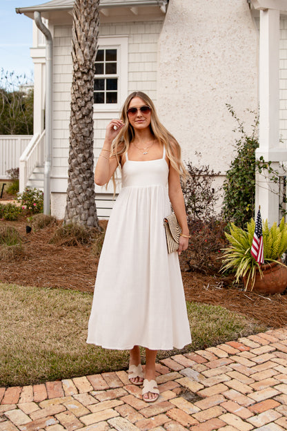 Woman in a white dress standing on a brick path in front of a white house.