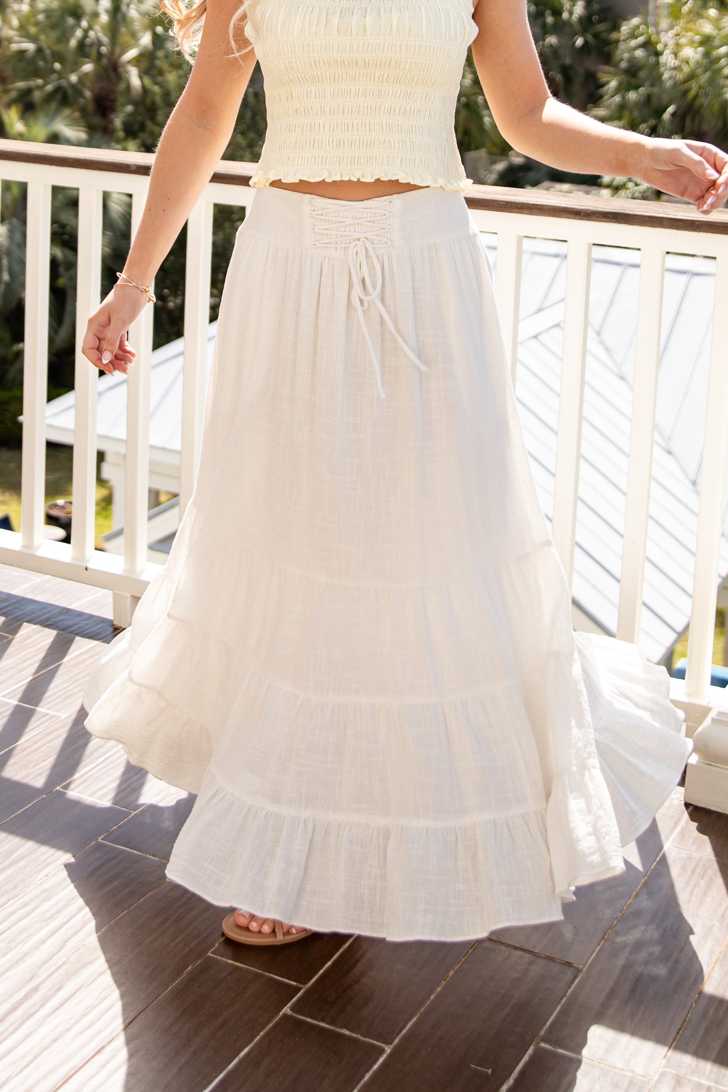 Woman wearing a white dress on a wooden deck with greenery in the background