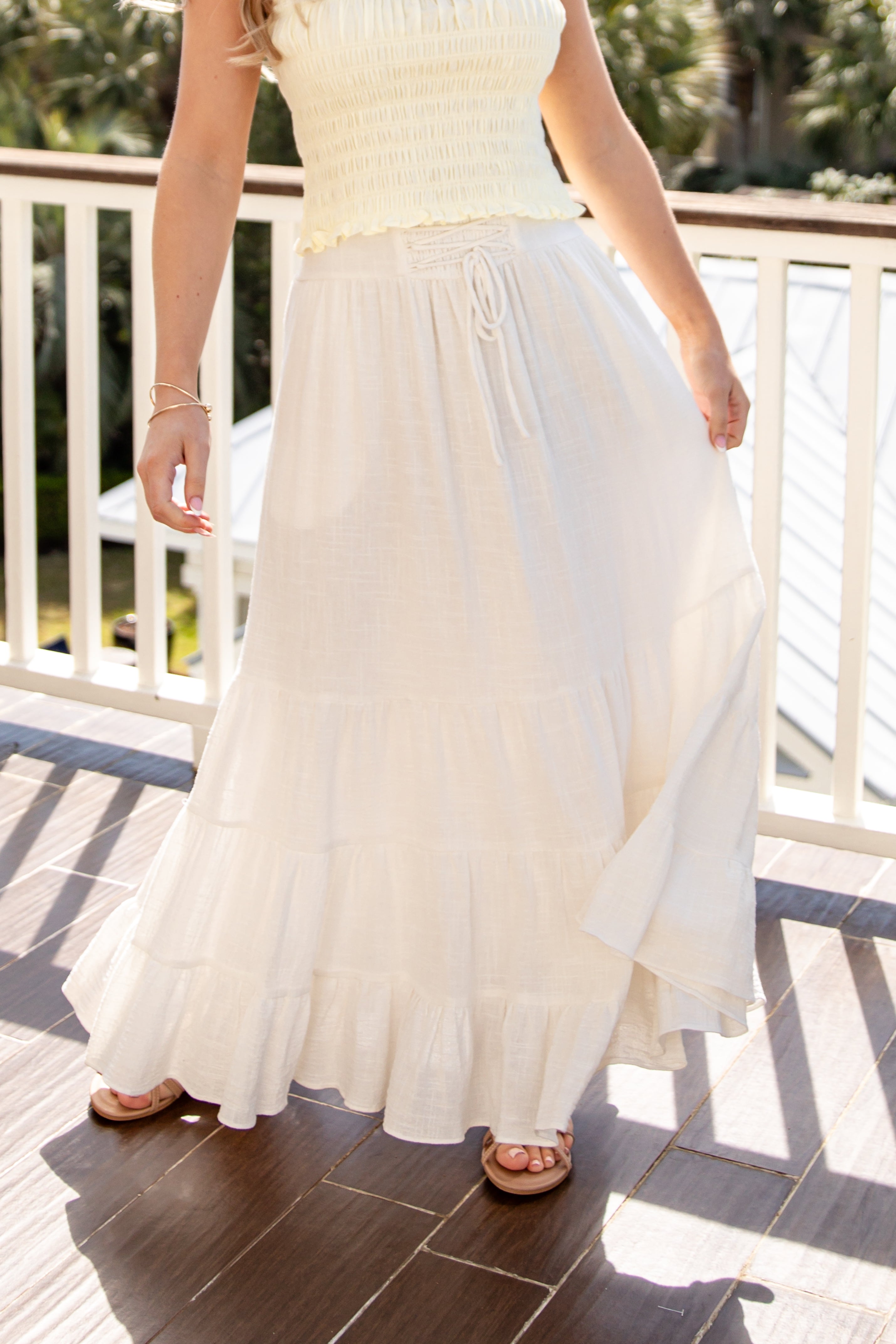 Person wearing a white dress on a balcony with greenery in the background