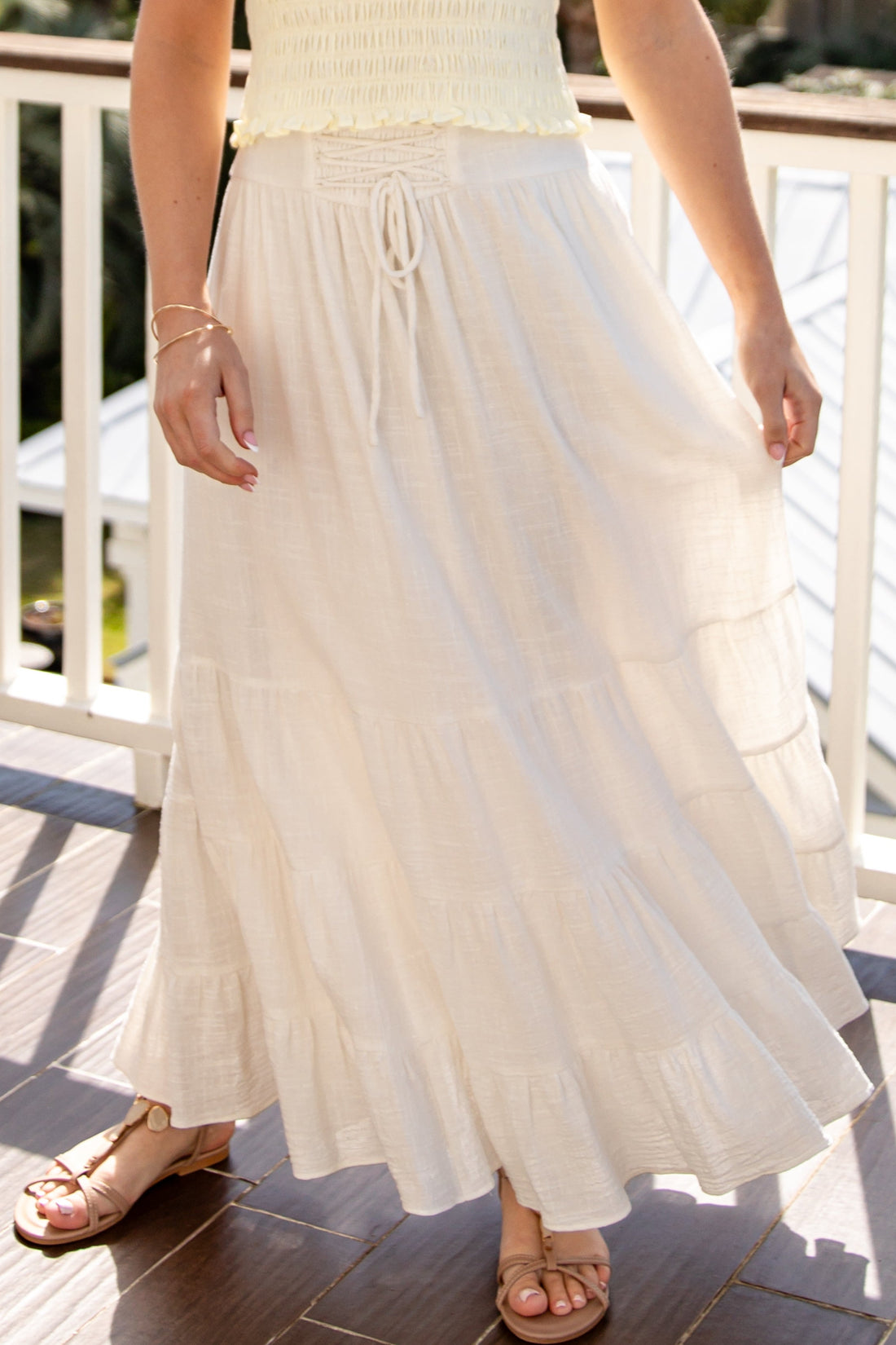 Woman wearing a white dress on a wooden deck with greenery in the background