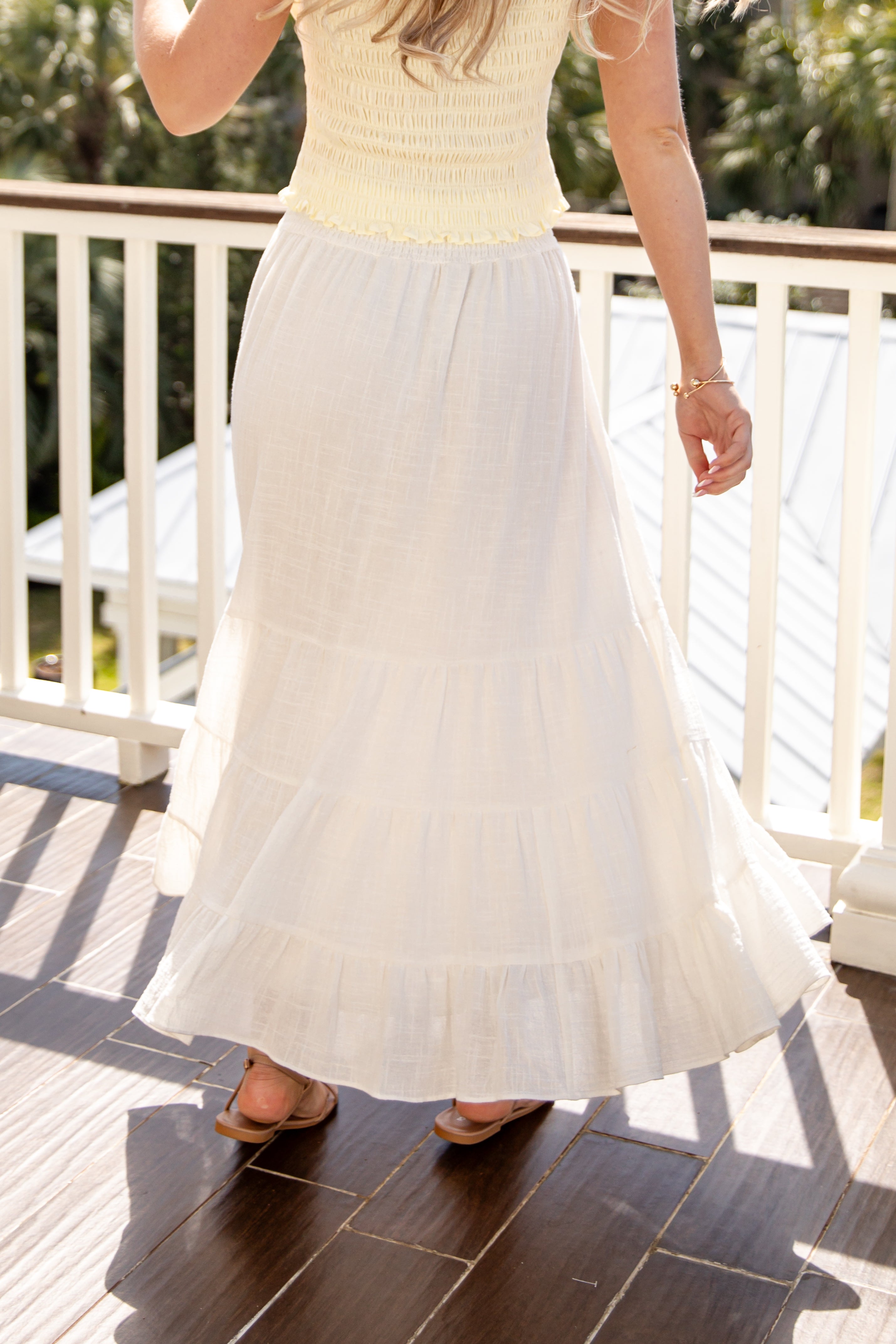Person wearing a light-colored top and white skirt on a wooden deck.