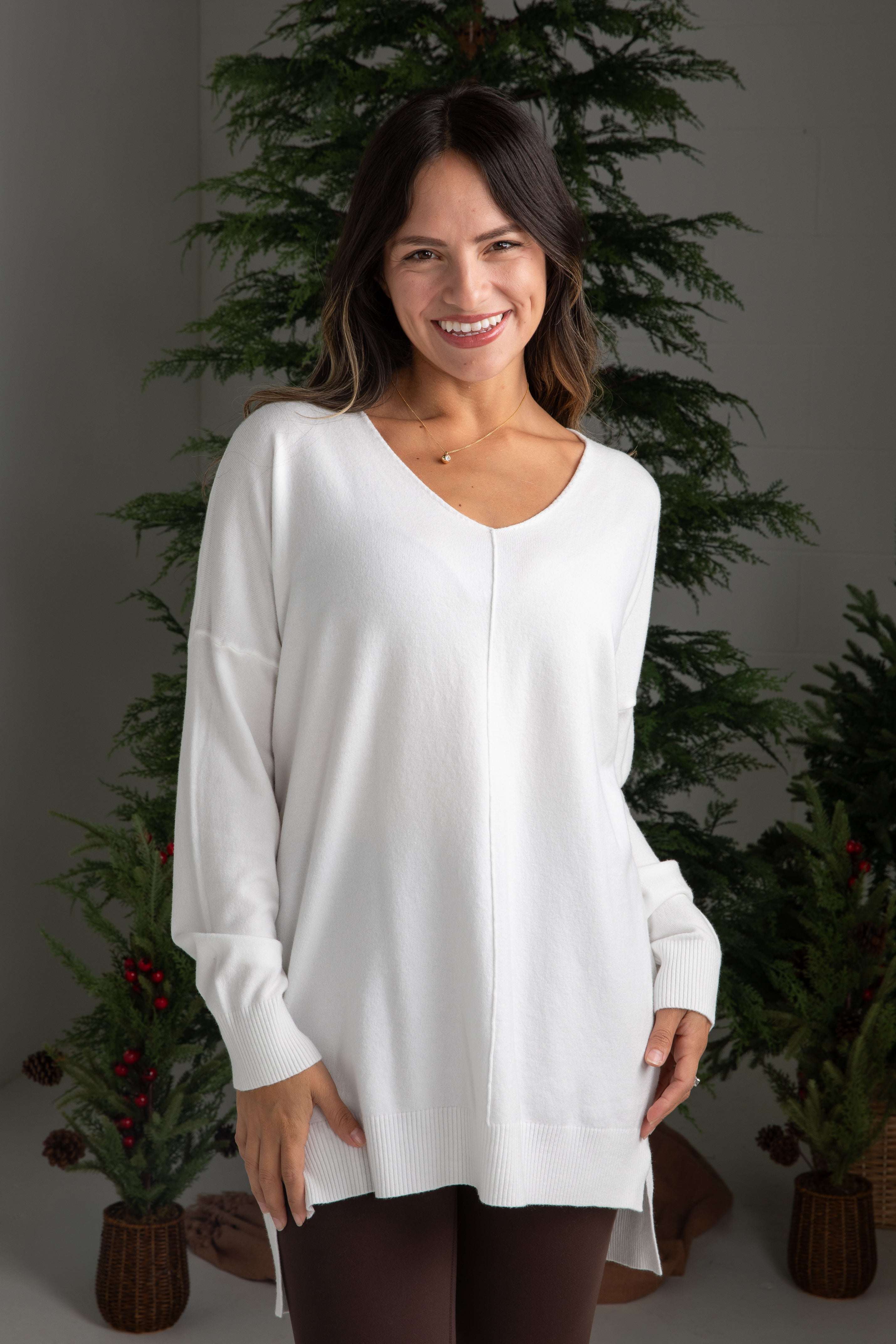 Woman wearing a white long-sleeve top in front of decorative plants.