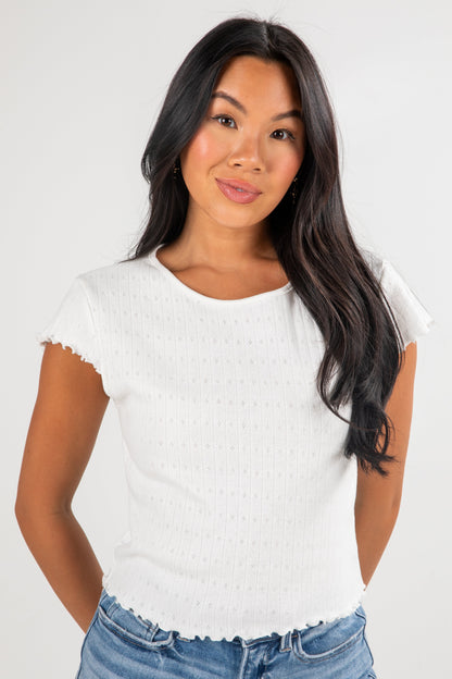 Woman wearing a white textured top and blue jeans on a plain background