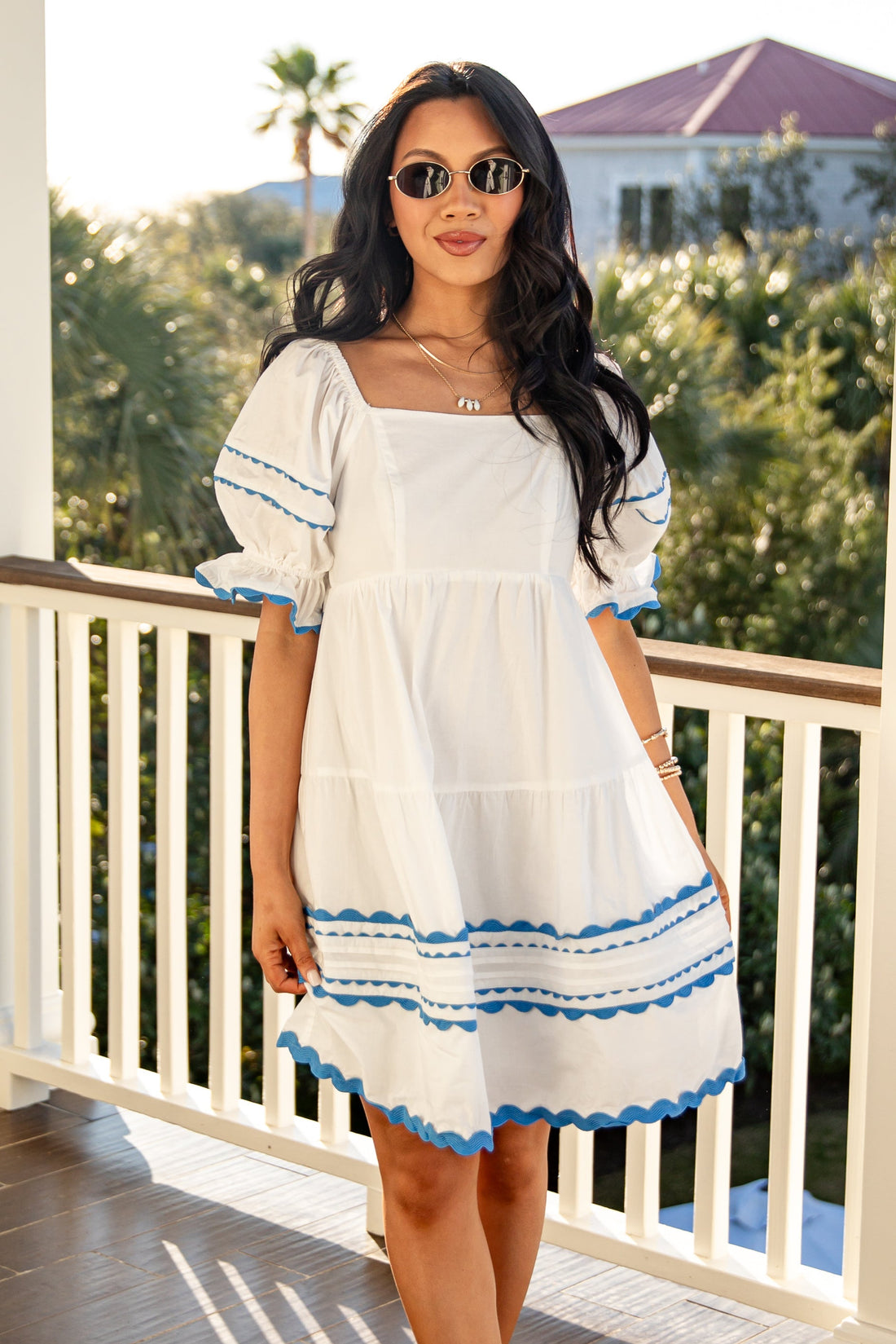 Woman in a white dress with blue trim standing on a porch.