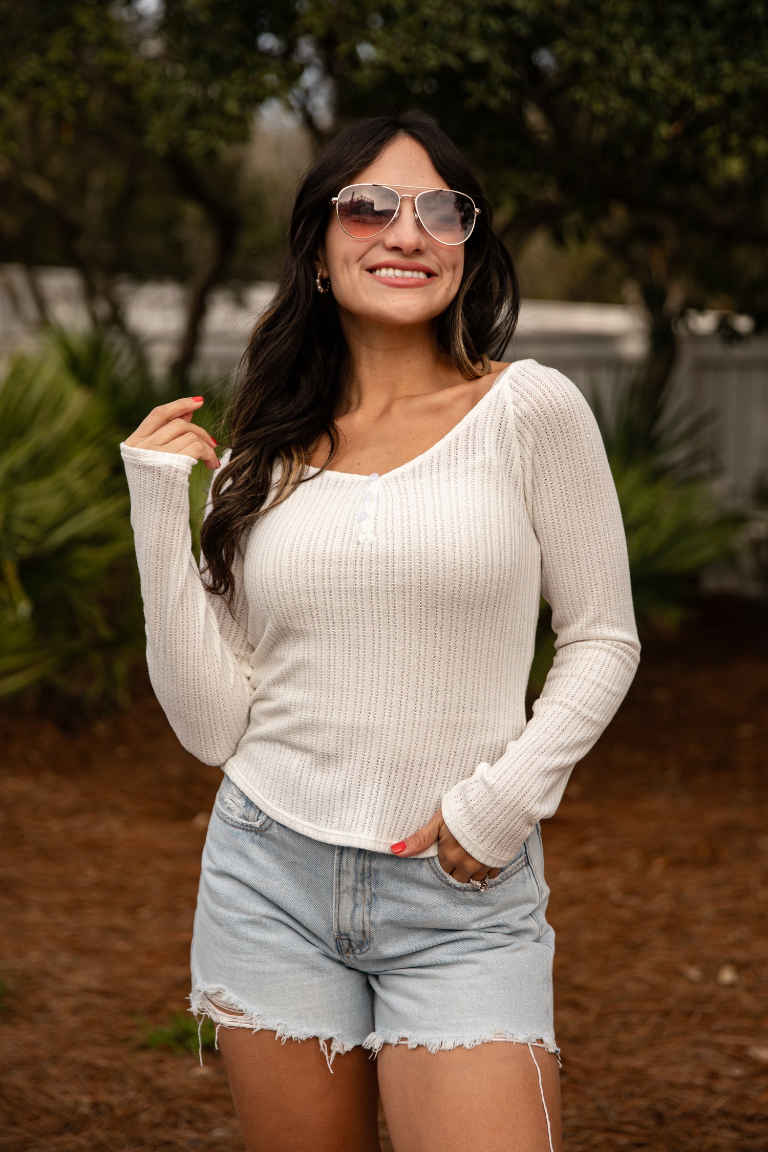 Woman wearing a white long-sleeve top and denim shorts outdoors.