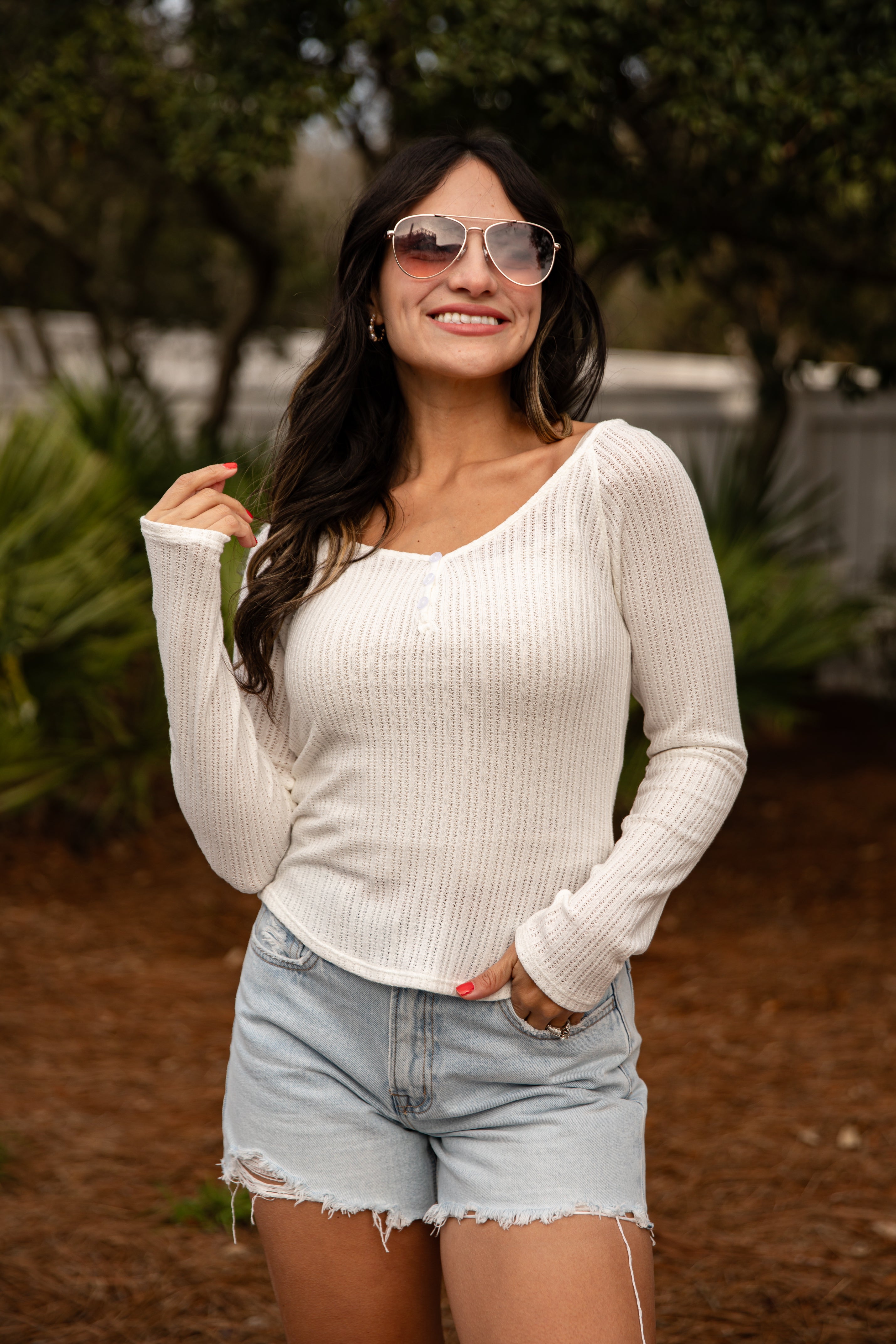 Woman wearing a white long-sleeve top and denim shorts outdoors.