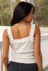 Woman wearing a white sleeveless top with ruffled straps on a blurred outdoor background