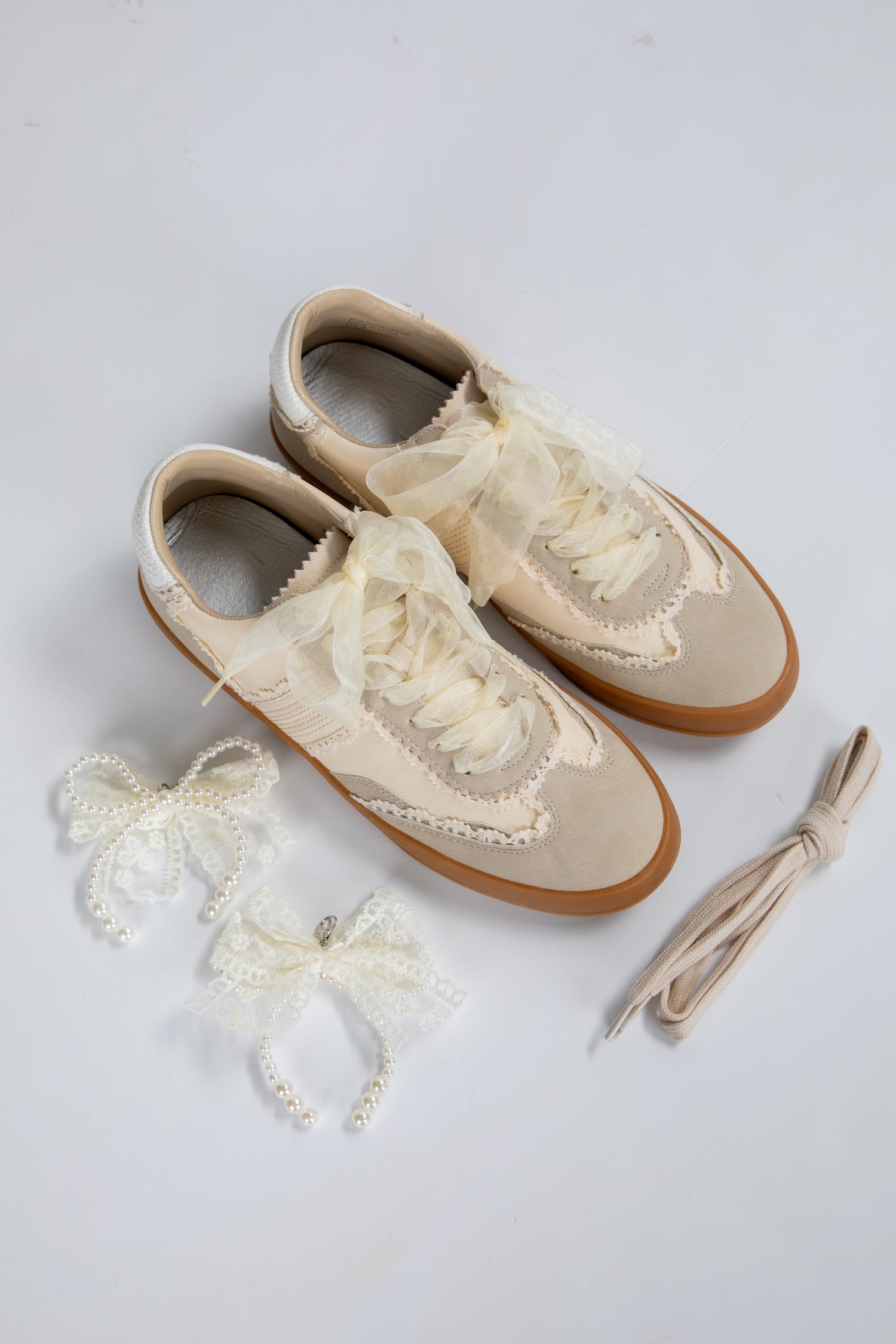 Pair of cream-colored shoes with lace details on a light gray background