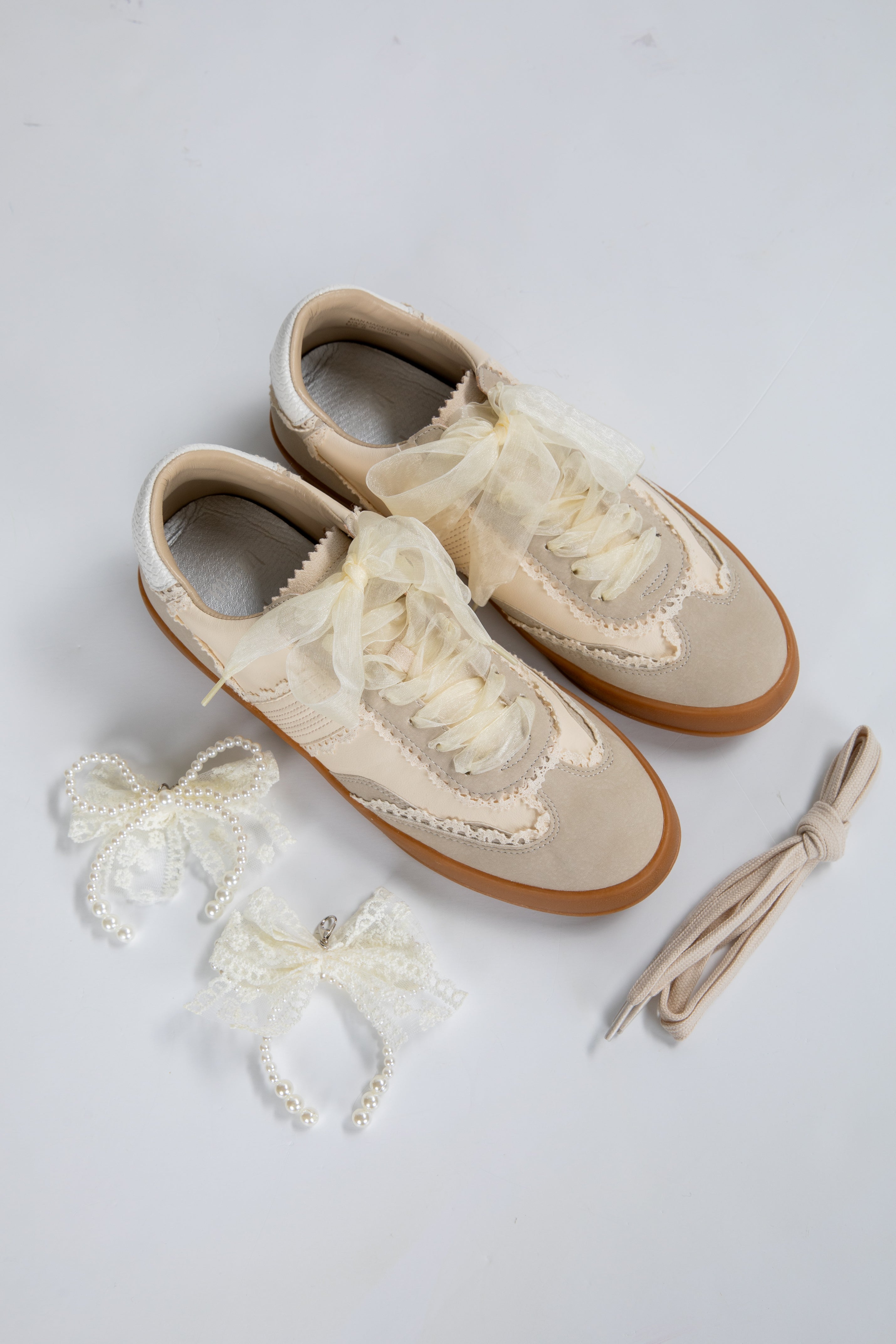 Pair of cream-colored shoes with lace details on a light gray background