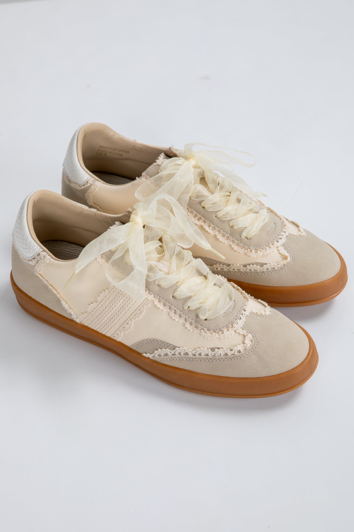 Pair of beige sneakers with white laces on a light gray background