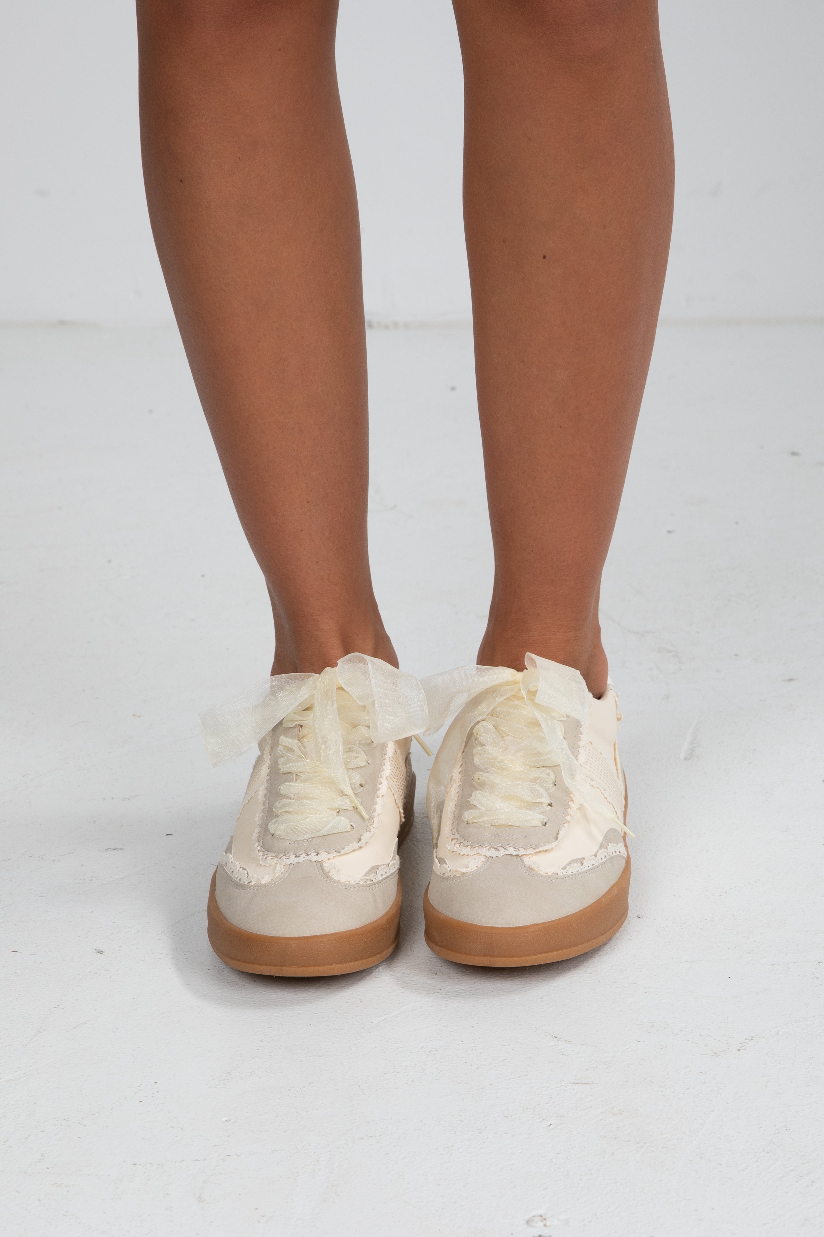 Beige sneakers with brown soles worn by a person on a white background