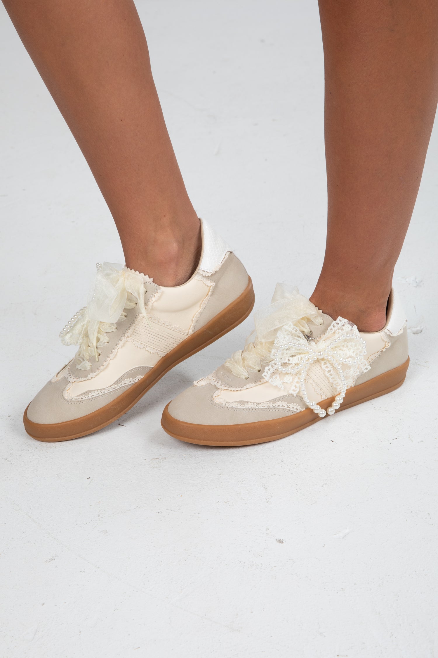 White sneakers with lace details worn by a person on a white background