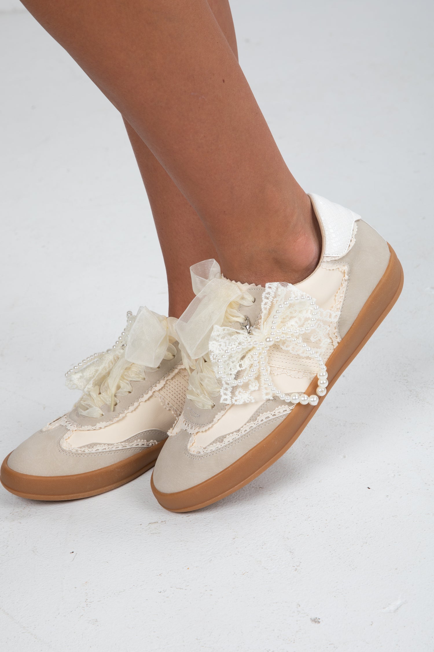 Beige sneakers with lace details worn by a person on a white background