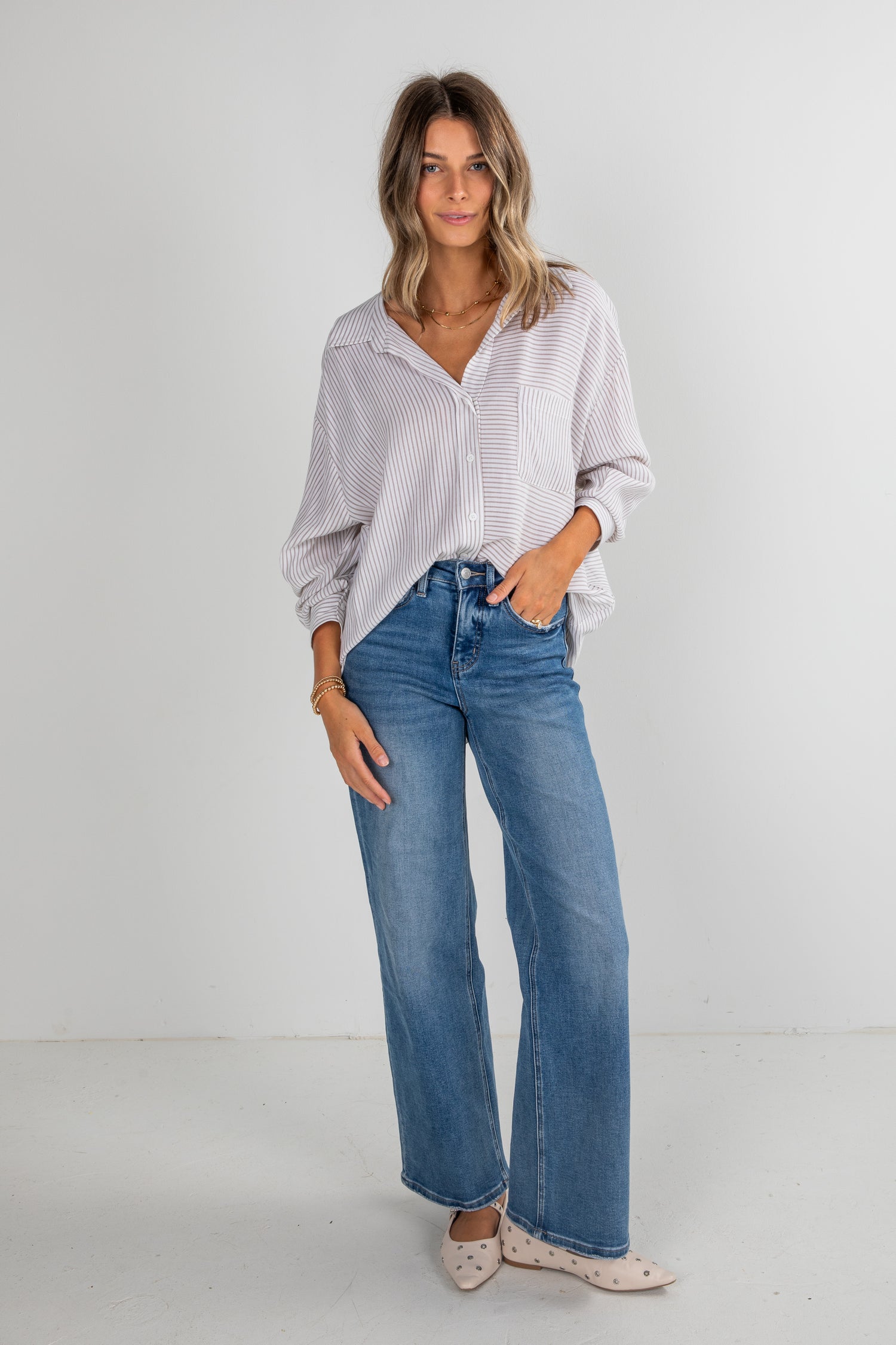 Woman wearing a white patterned shirt and blue jeans on a plain background