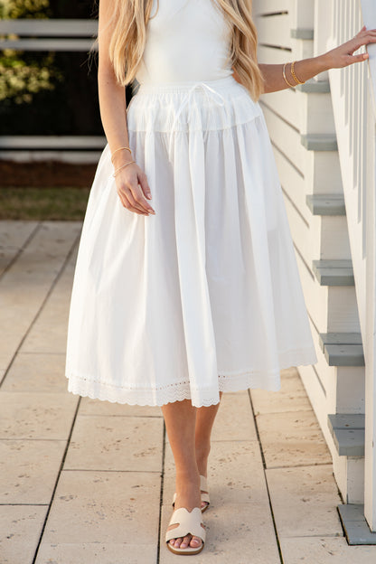 Woman wearing a white skirt standing on a wooden deck.