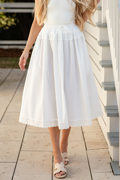 Woman wearing a white skirt standing on a wooden deck.