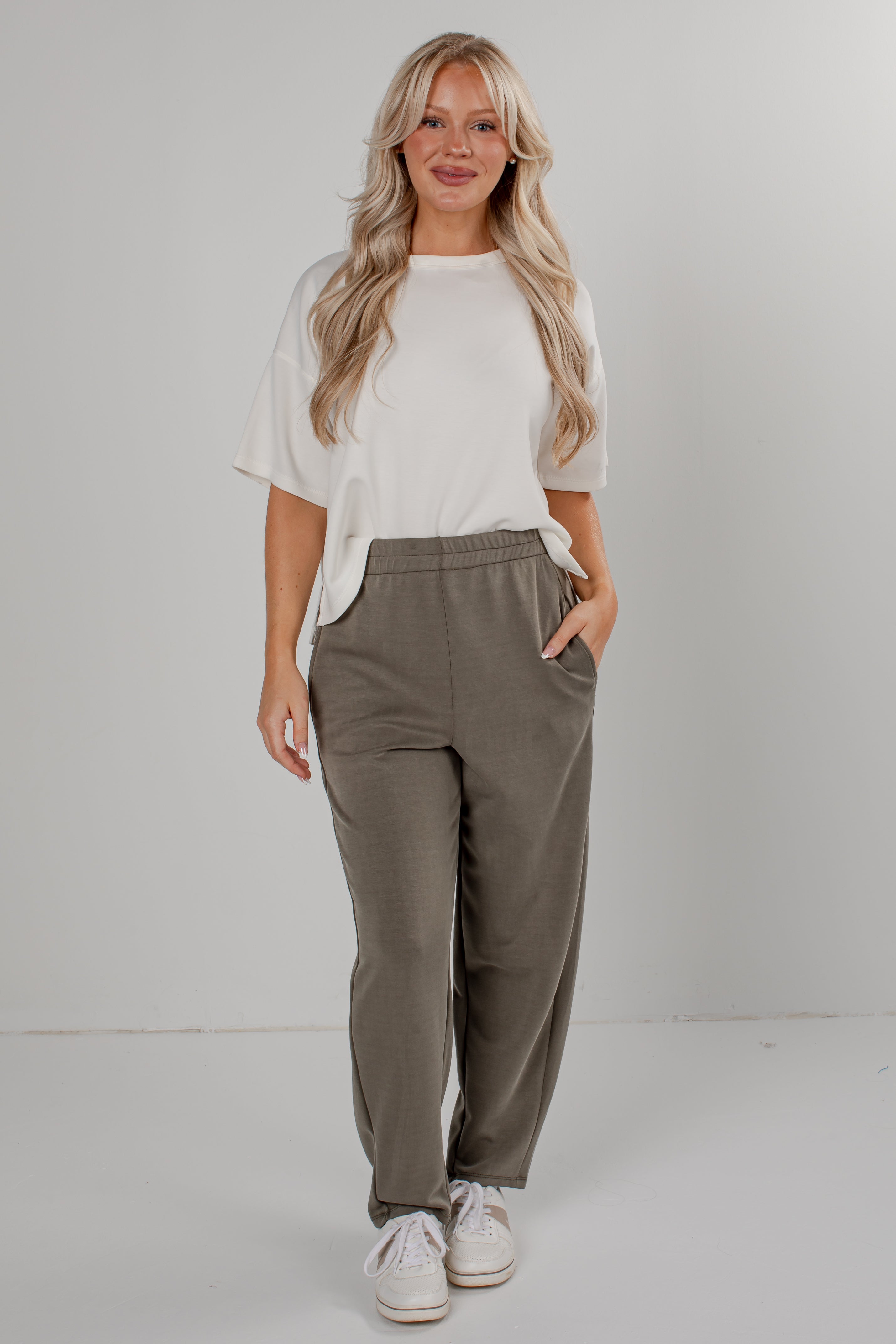 A woman modeling a white short-sleeve t-shirt and olive green wide-leg sweatpants, standing against a light gray studio background.