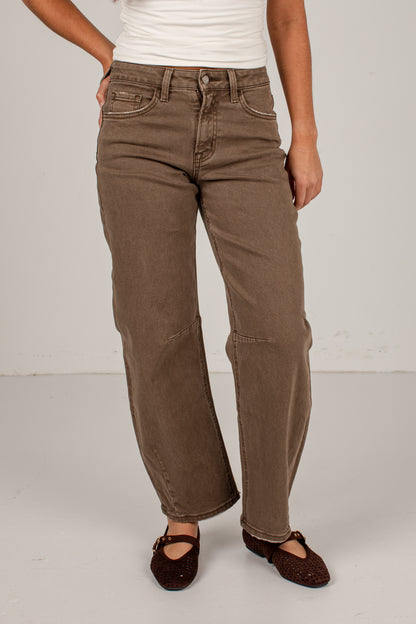 A person wearing brown wide-leg corduroy pants, styled with a white top and dark brown Mary Jane shoes, standing against a light gray studio background.