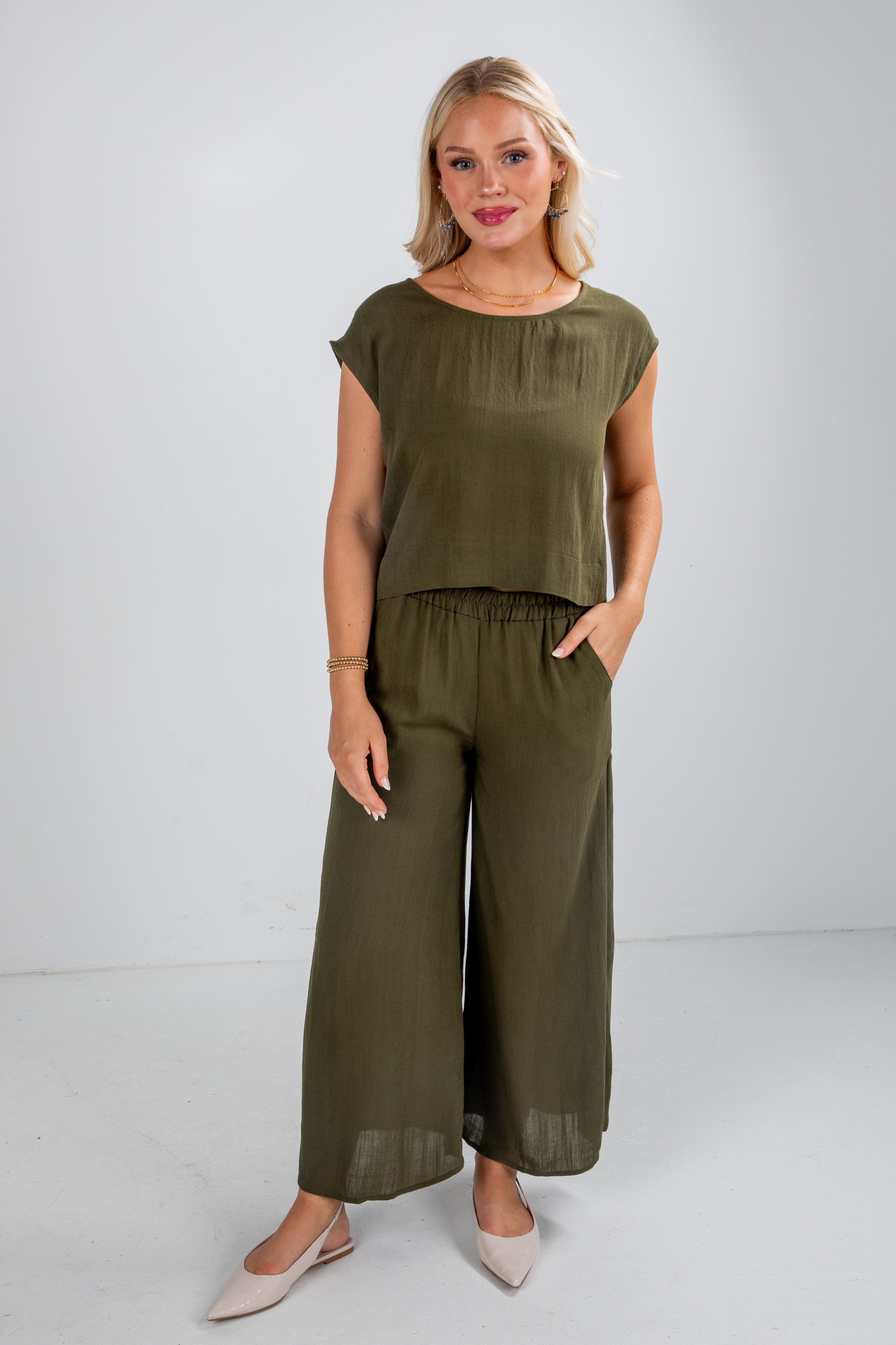 Woman wearing an olive green outfit with wide-leg pants on a white background