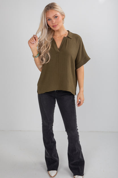 Woman wearing an olive green blouse and black pants on a white background