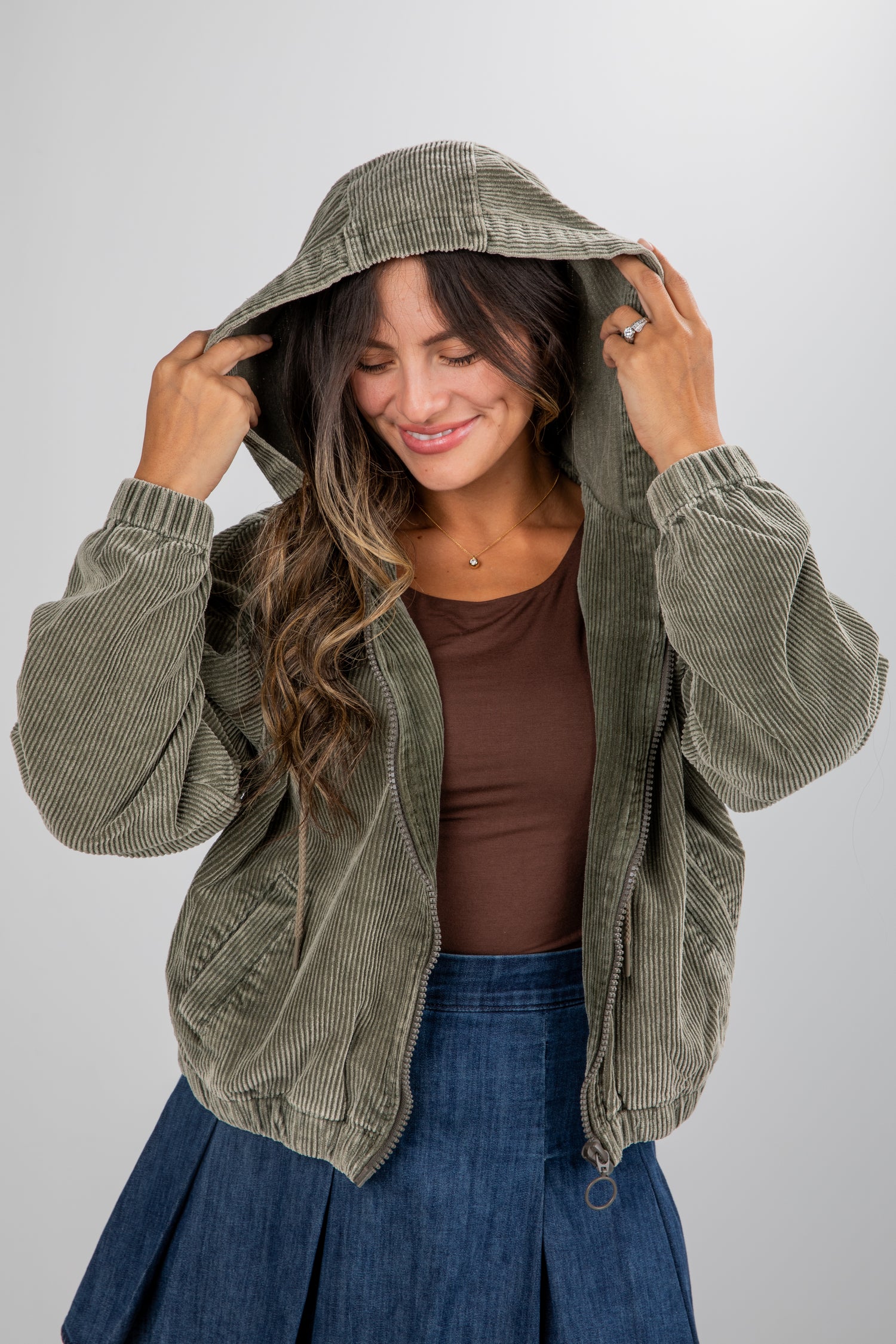 Woman wearing a green corduroy jacket with a hood against a white background