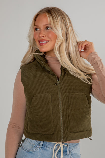 Woman wearing an olive green vest against a plain background