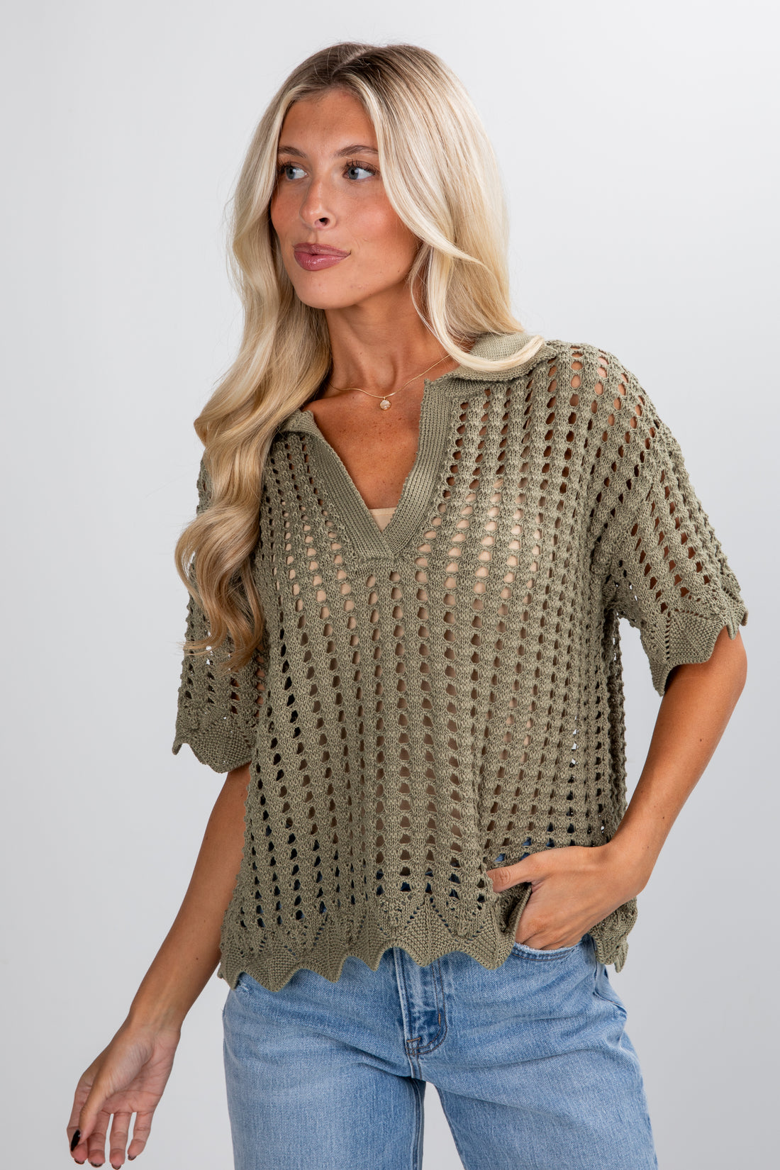 Woman wearing a green crochet top and blue jeans on a plain background