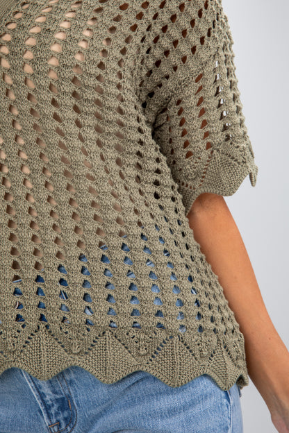 Close-up of a person wearing a green crochet top with a white background