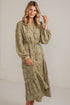 A woman modeling a long-sleeved olive green and beige patterned midi dress with a tie waist, standing in a bright white studio setting.