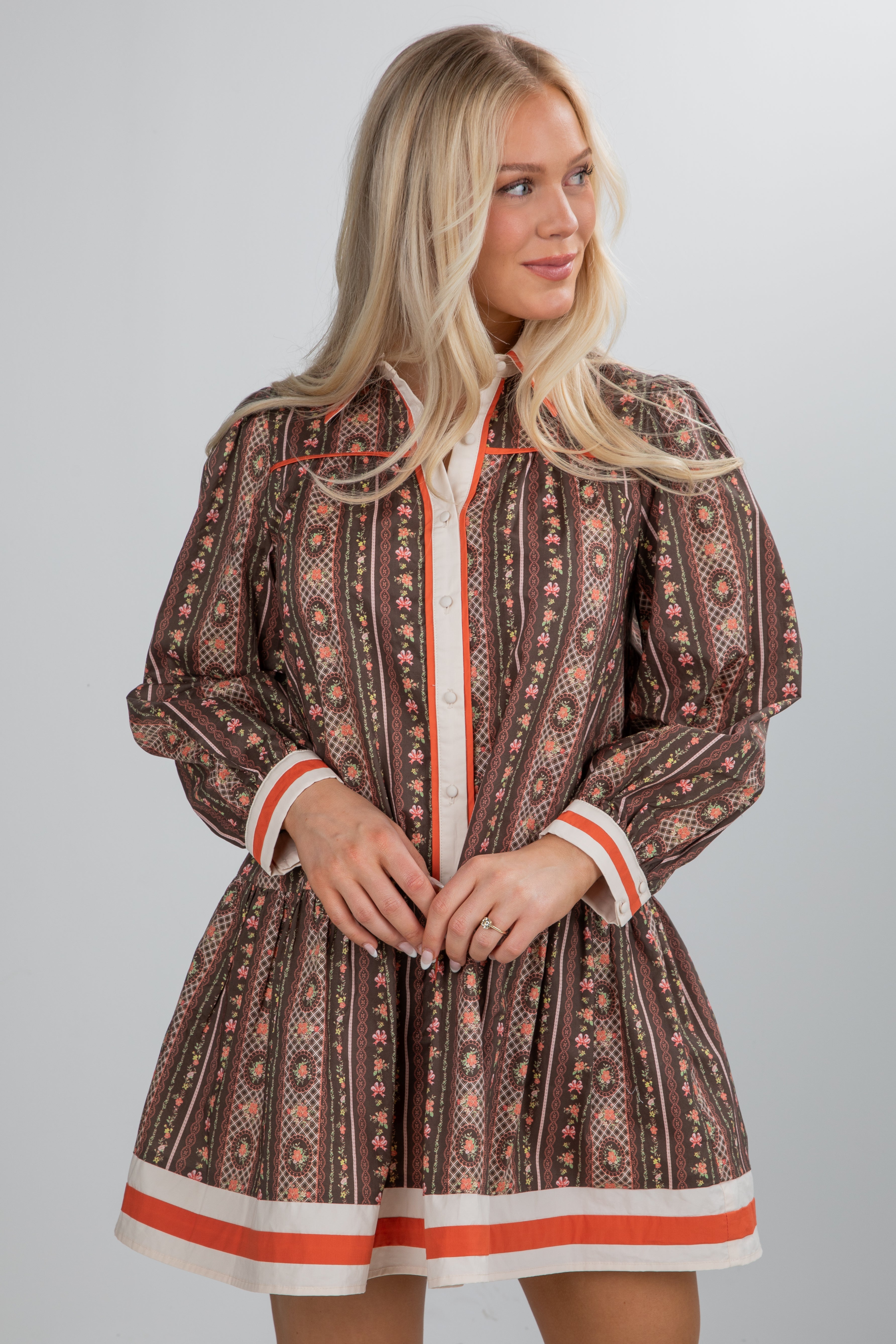 Woman wearing a patterned dress with orange accents on a gray background